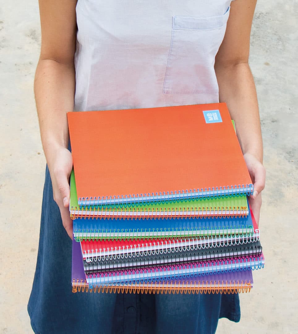 Persona sosteniendo una pila de cuadernos de colores diseñados por Nomon Design, agencia de branding, para Miquelrius.