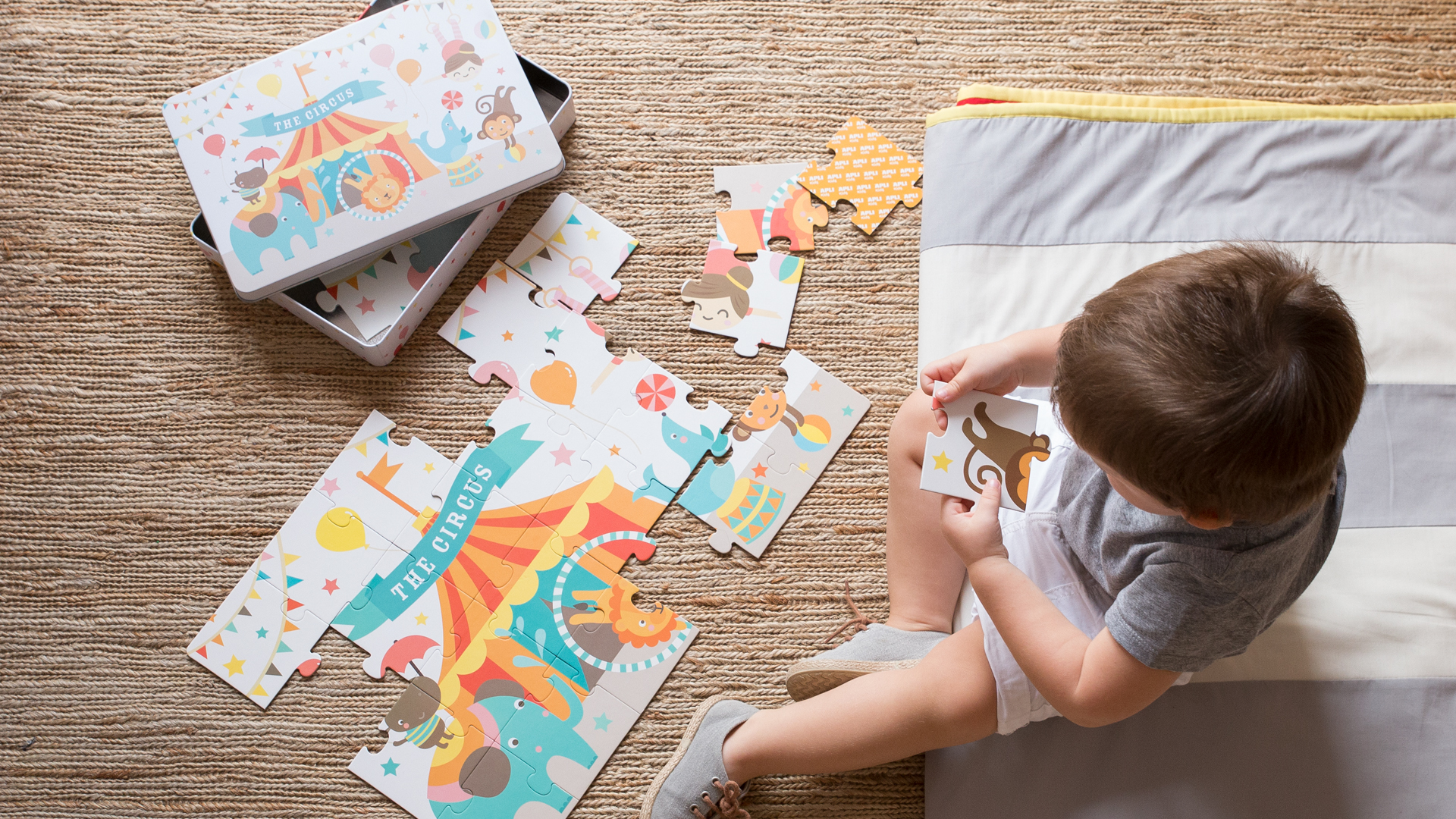 Niño jugando con puzzle del circo de Apli Kids en caja metálica ilustrada, diseño de Nomon Design, agencia de branding