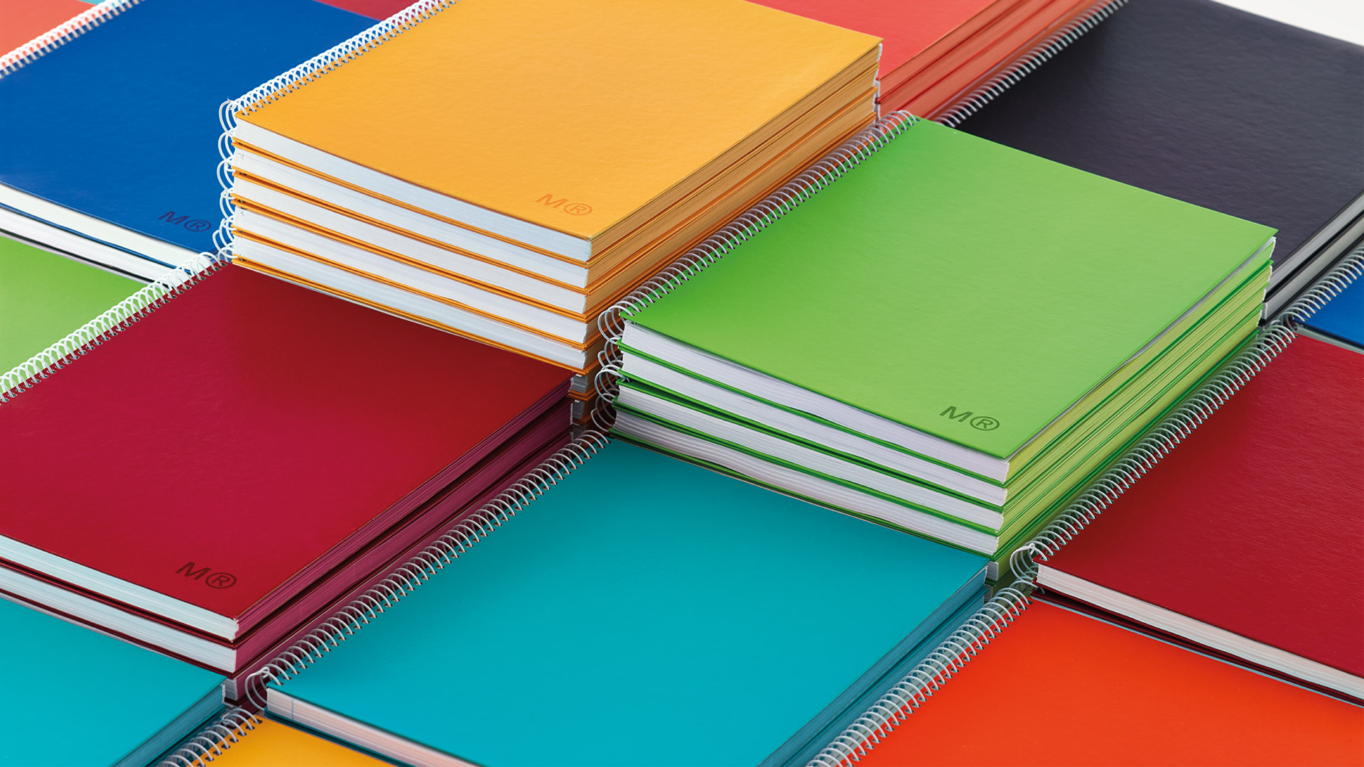 Cuadernos de colores Miquelrius diseñados por NOMON DESIGN alineados sobre fondo neutro con pies en plano cenital
